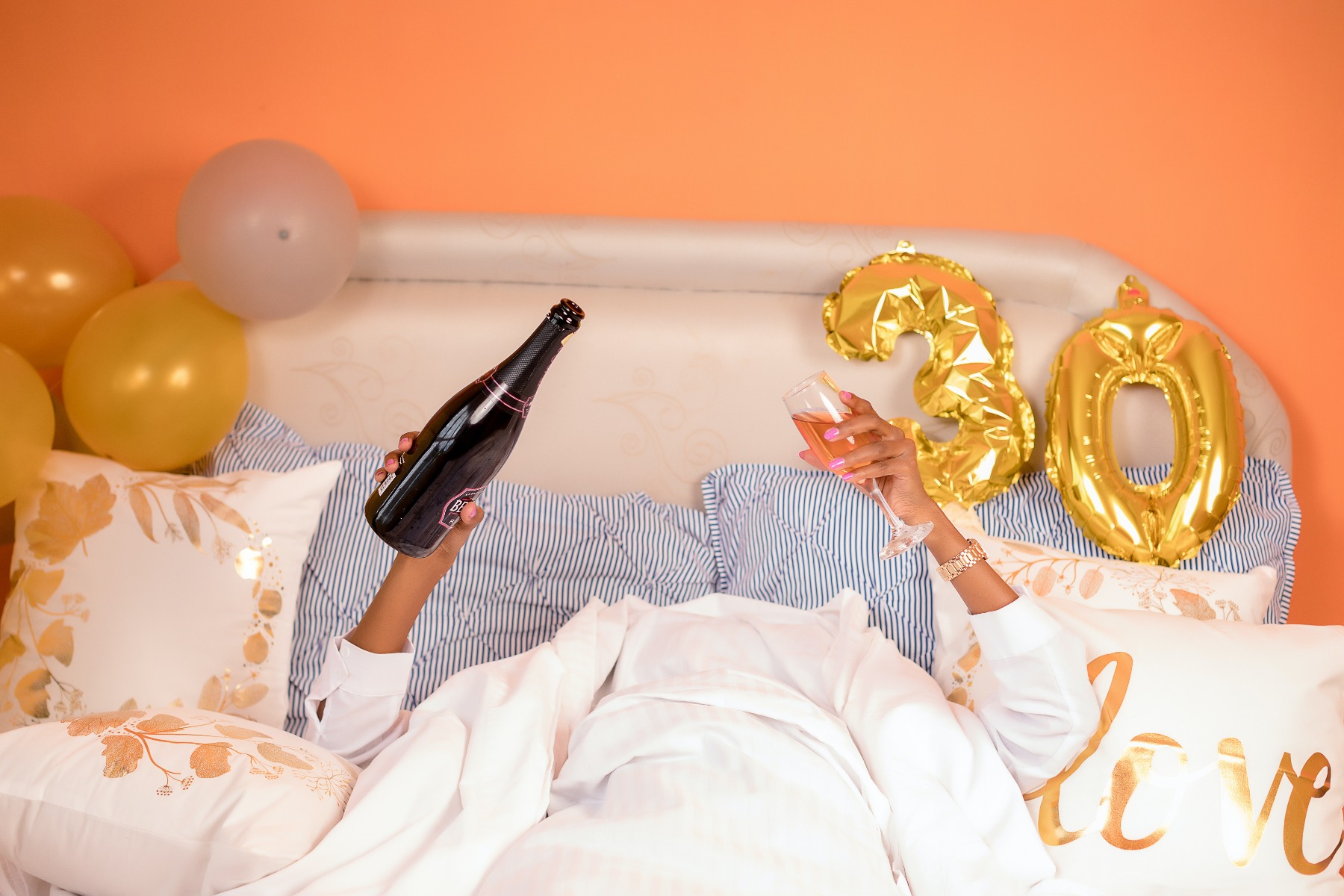 Femme dans son lit le lendemain de ses 30 ans, coupe de champagne et bouteille en main